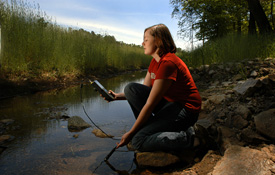 Student testing water at a stream.