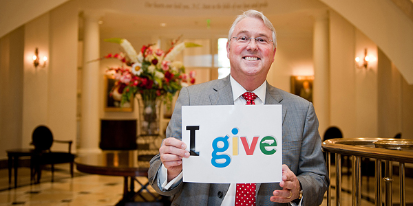 Chancellor Woodson with a sign reading, "I Give."
