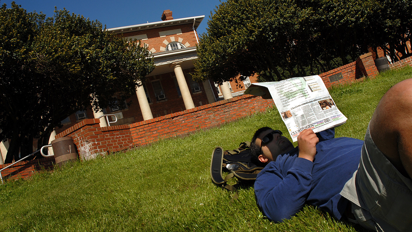 College of Education junior Greg Capobianco reads Technician while lying on the grass in front of the 1911 building.