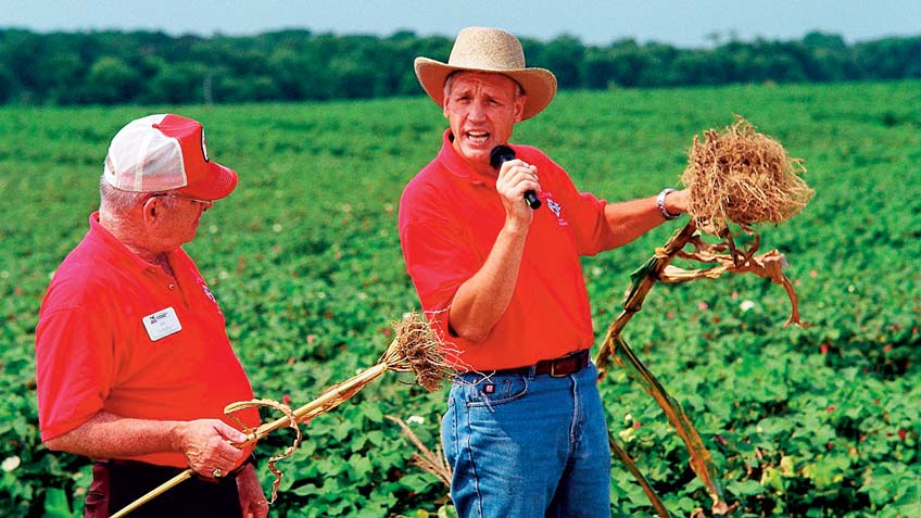 Ron Heiniger holding a microphone as he explains farming to an audience in a field.