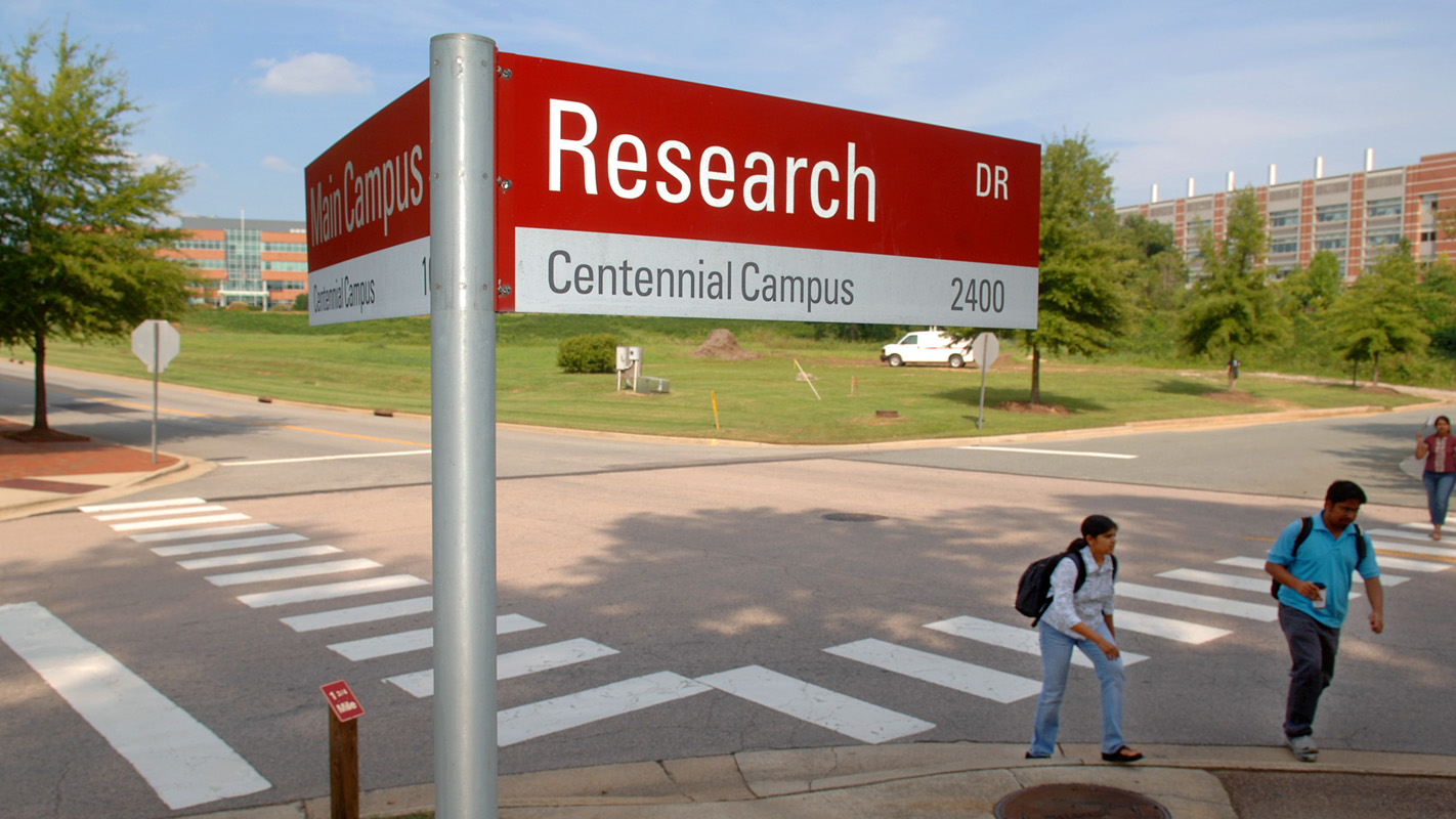 Street sign on Centennial Campus with students walking.