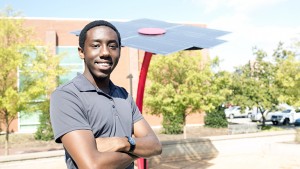 NC State computer science graduate Xavier Primus stands in front of a 16-foot solar sculpture.