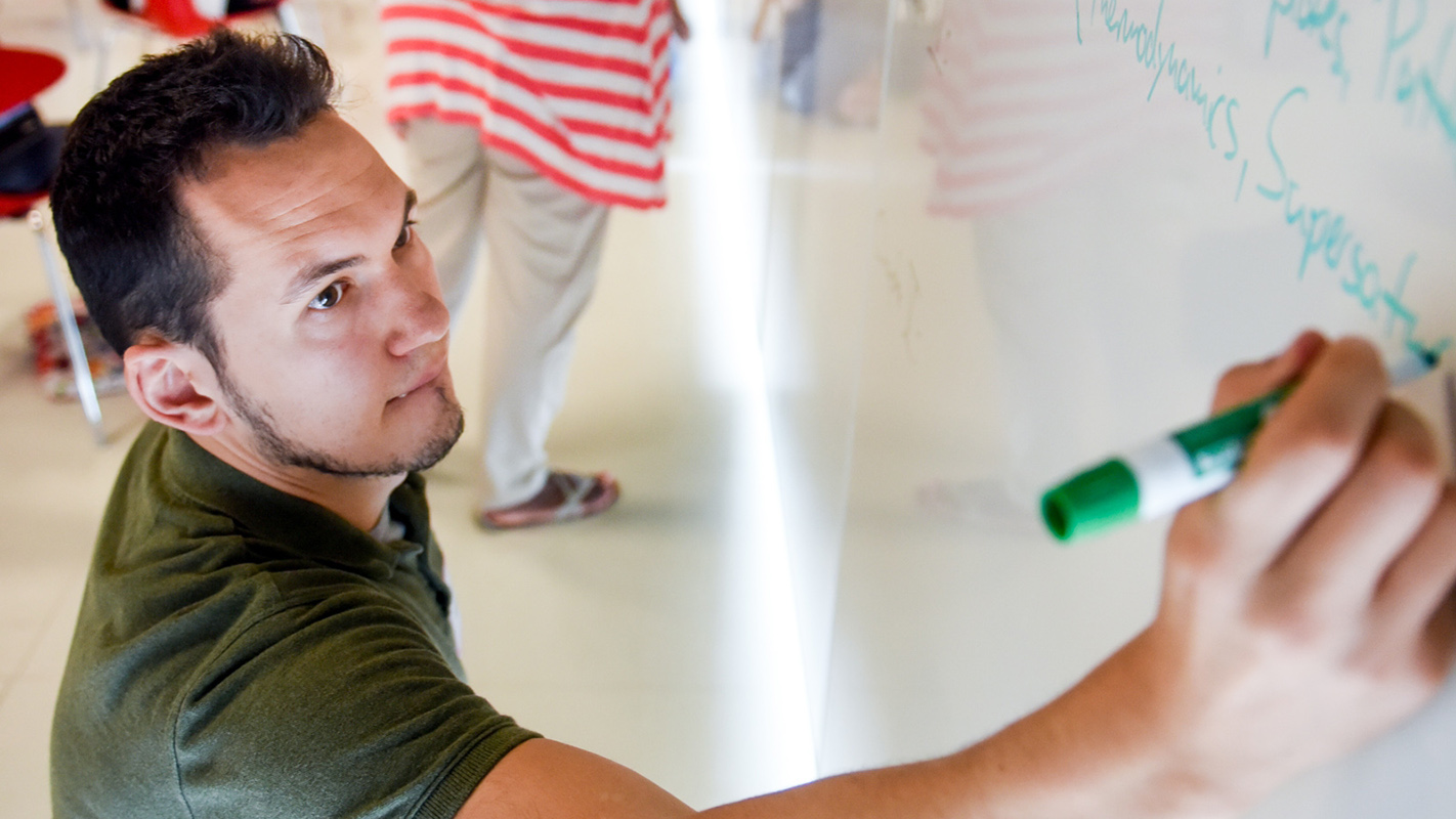 A man in a green shirt writes on a whiteboard at NC State's Dissertation Institute.
