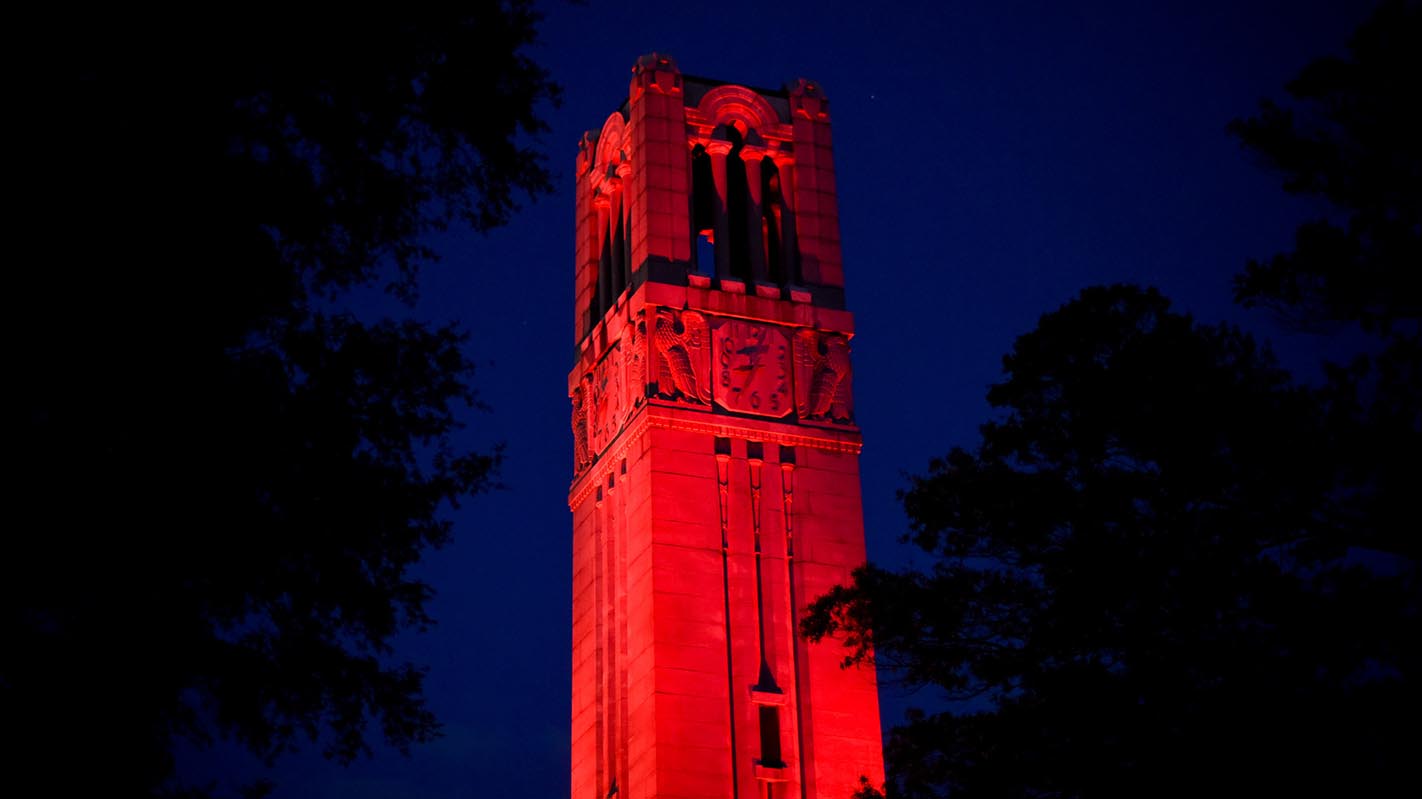 The Memorial Belltower at NC State lit in red to celebrate faculty excellence.