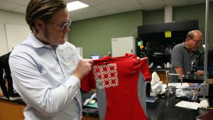 A man in a research lab holds up a red wearable tech T-shirt.