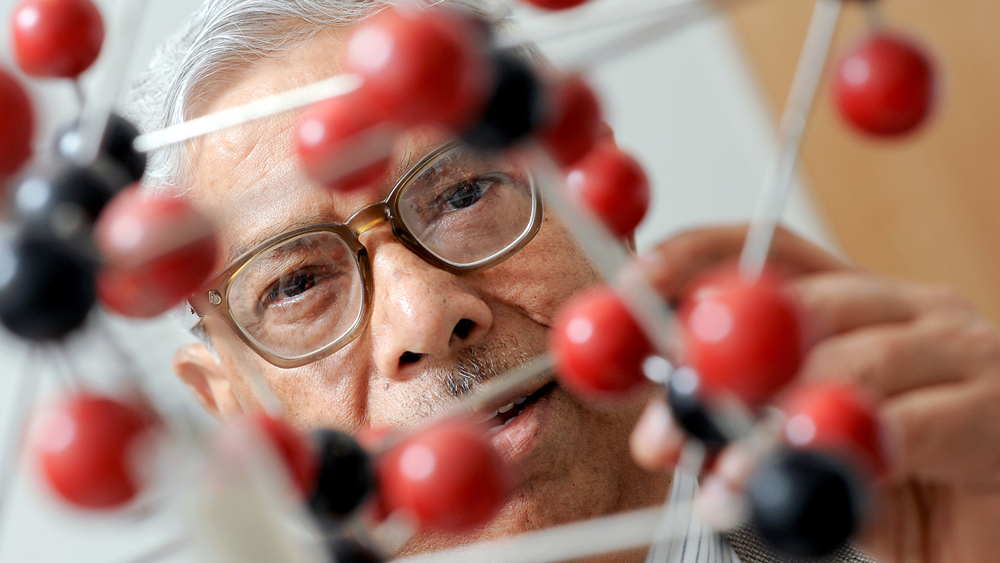 An NC State professor in materials science and engineering half-hidden behind a 3-D molecule.