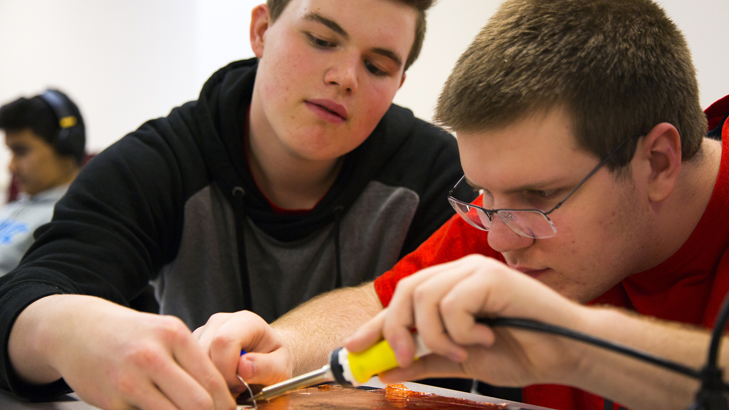 Two Catalyst program students work on soldering a circuit.