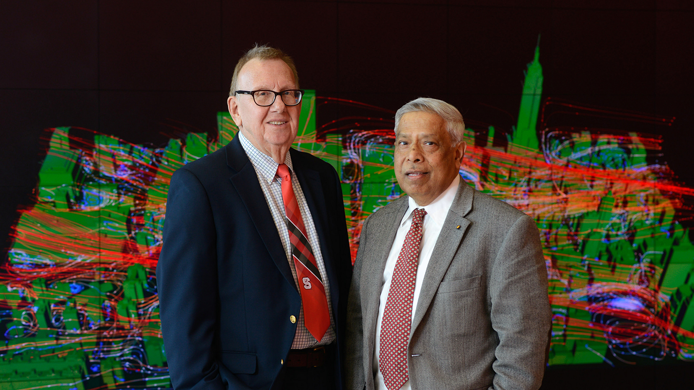 Two engineers professors pose together in front of a visualization wall at the Hunt Library.