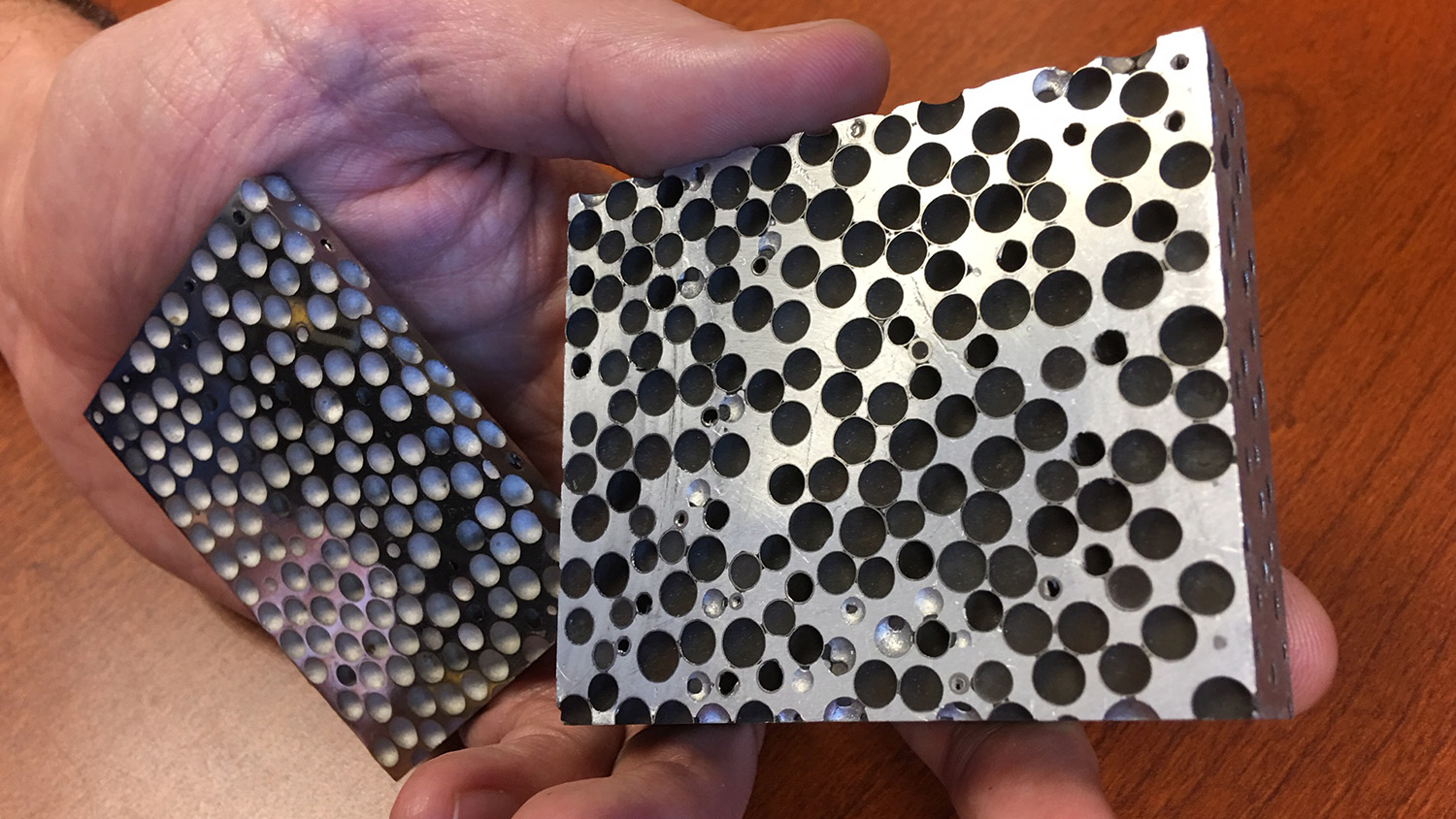 A person holds two small blocks of silver metal foam.
