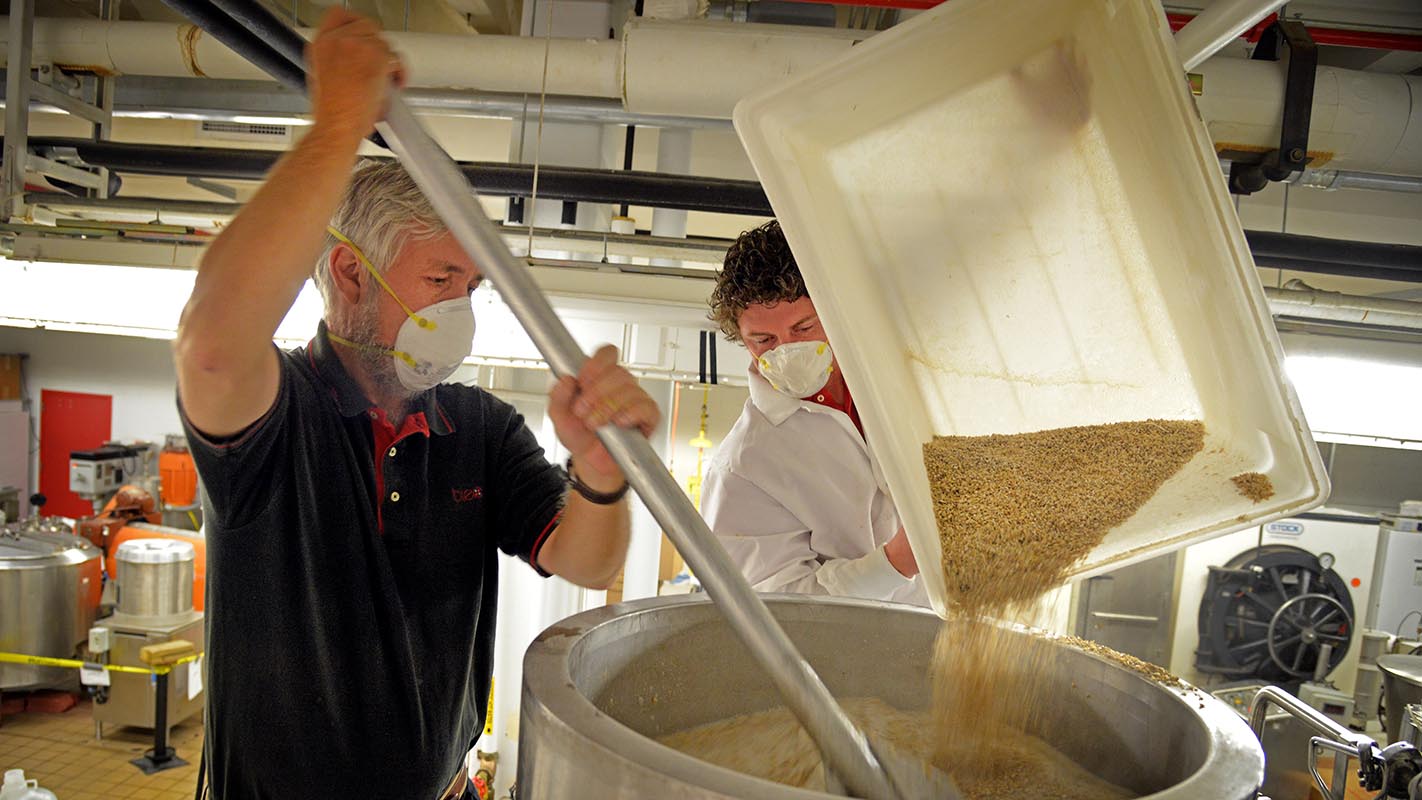 Dr. John Sheppard, coordinator for the undergraduate Bioprocessing Science Program, stirs malt while student Brandon Jackson (right) pours in the brewing lab at Schaub Hall.