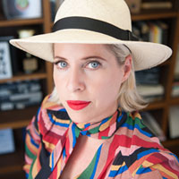 Close up shot of Tiffany Shlain wearing a white bowler hat and bright red lipstick.