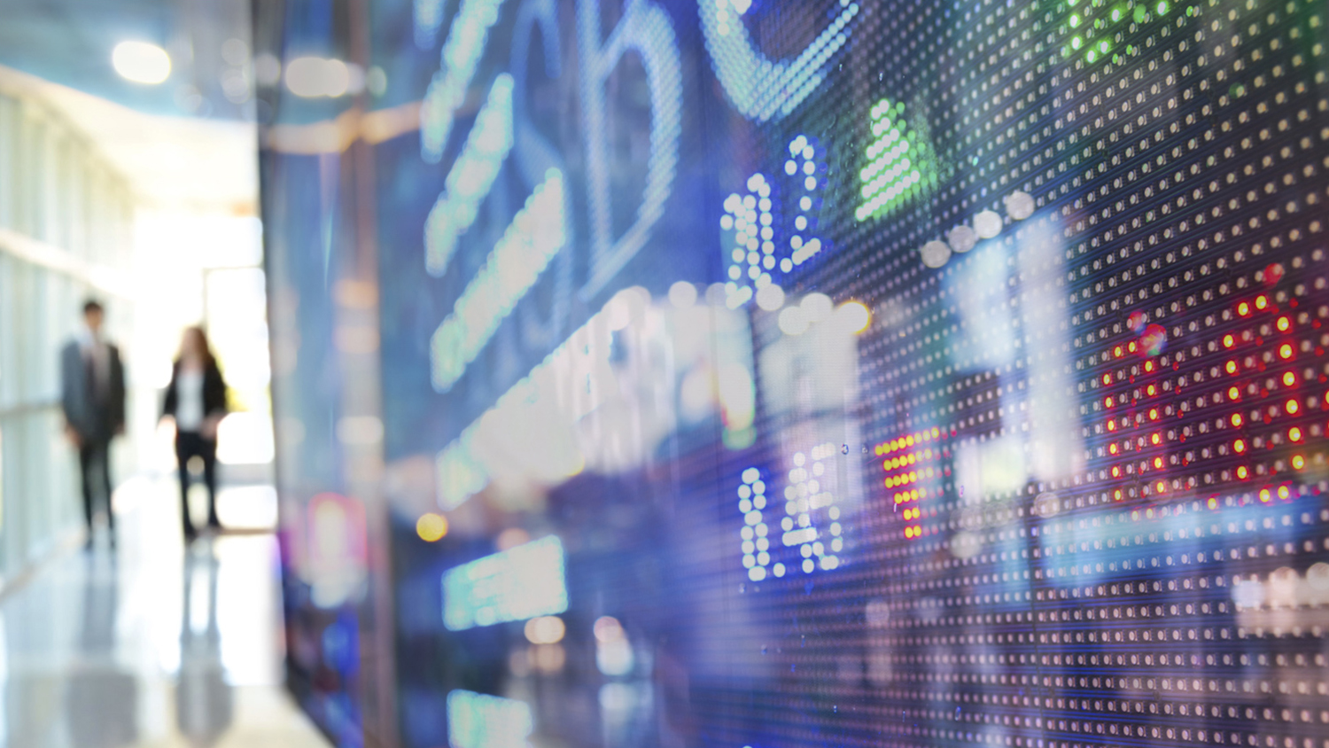 Two business people walk past a stylized stock ticker in the foreground.