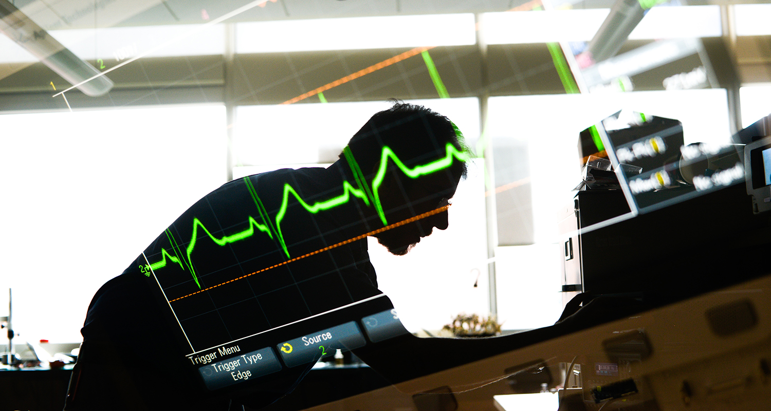 Researcher bent over a lab table with image of heart monitor superimposed.