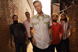 Members of the band American Aquarium look at the camera. The lead singer is flanked by four bandmates as the late evening sun glows behind them.