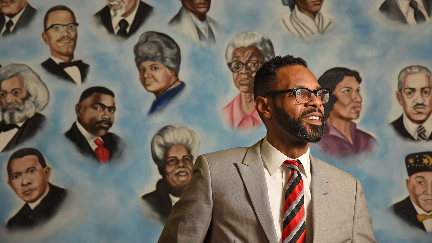 Moses T. Alexander Greene standing against a mural with pictures of black historical figures.