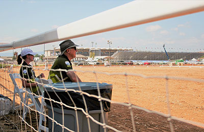 A man and a woman sitting on chairs just inside a horse track