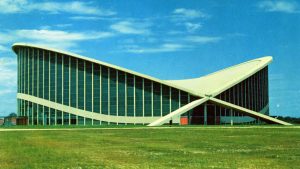 The curving, modern Dorton Arena is seen on a green expanse of lawn in a postcard image from the 1950s.