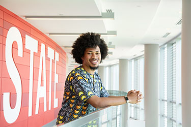 John Miller IV standing in front of a sign that reads NC State.