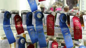 Dozens of jars of preserves sport long, satiny blue and red ribbons.