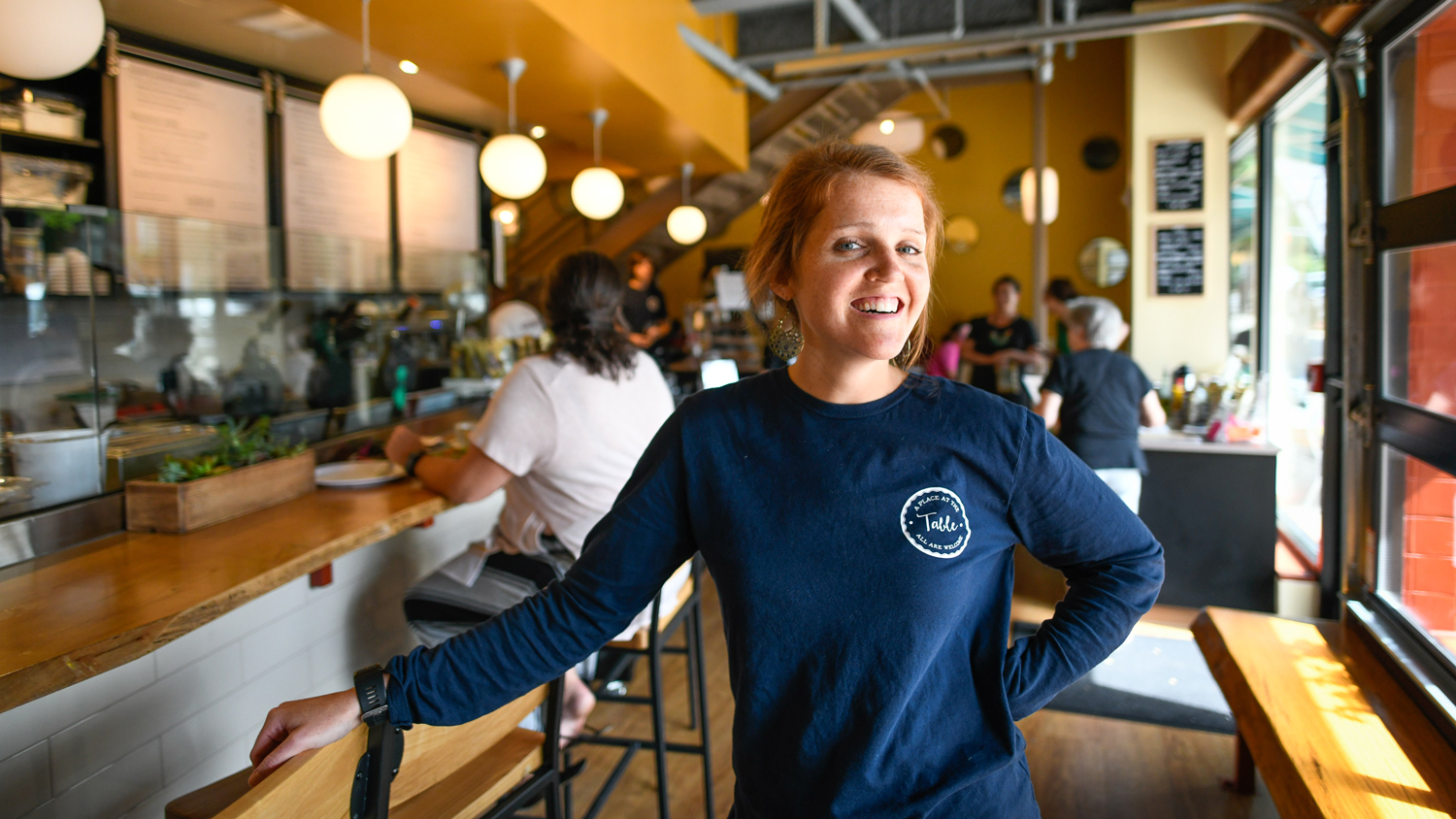 A woman stands in front of her restaurant's counter.