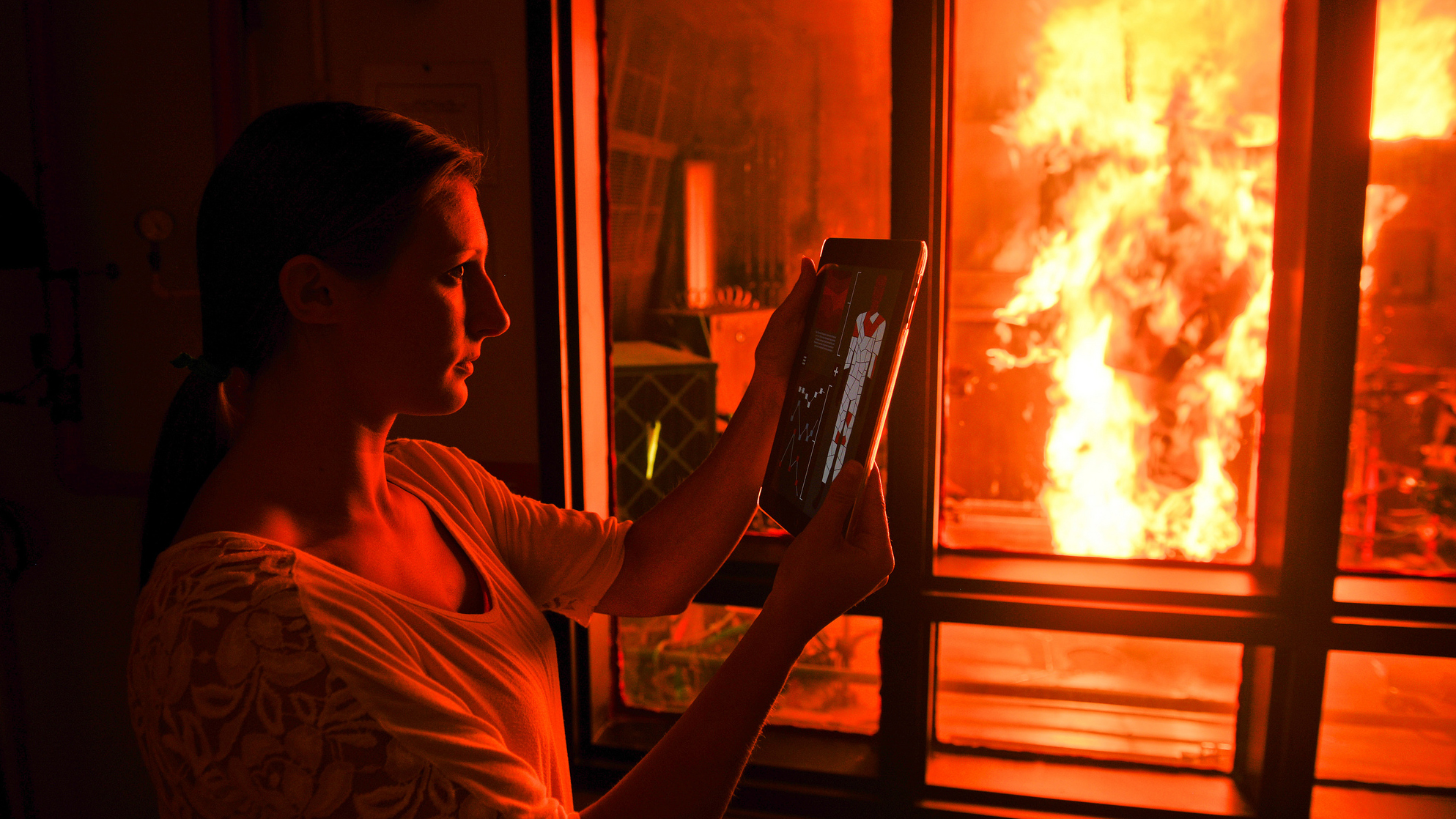 A researcher looks at results on an iPad while the PyroMan manikin is aflame in a glass chamber