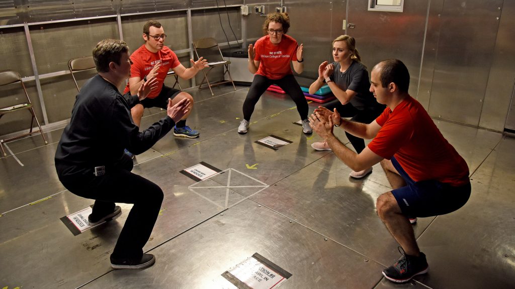 Five people wearing athletic clothing squat in a small room to test fabric