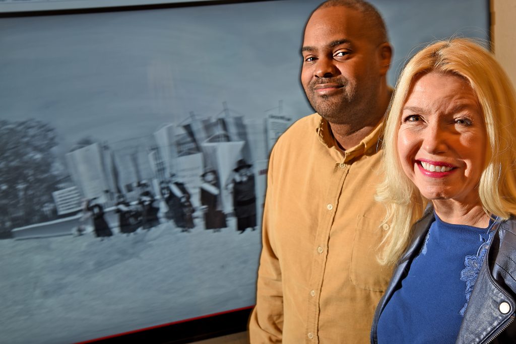 Derek Ham, assistant professor of graphic design, and Melanie Graham, lecturer in the Department of English, stand in front of a monitor displaying an excerpt from the Our Voices Will Be Heard VR presentation.