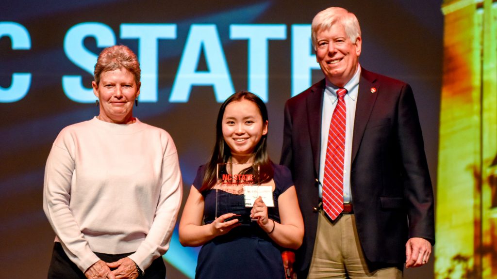 Tea Blumer holding her award onstage at the Lulu eGames. Kathy Hengen, COO of Lulu is at left, and Tom Miller, senior vice provost for academic outreach and entrepreneurship, is at right.