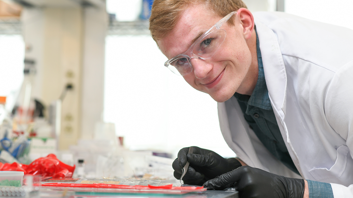 Neil Baugh leaning over his lab bench, smiling at the camera.