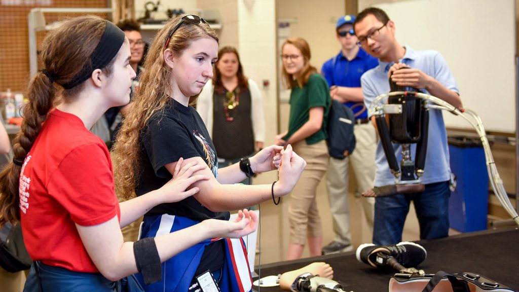 Two high school students with sensors on their forearms and a prosthetic foot in the background