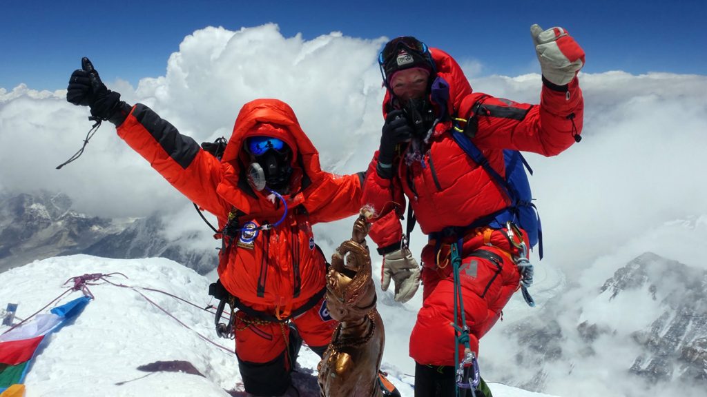 Two climbers at the top of Everest, giving a thumbs-up signal.