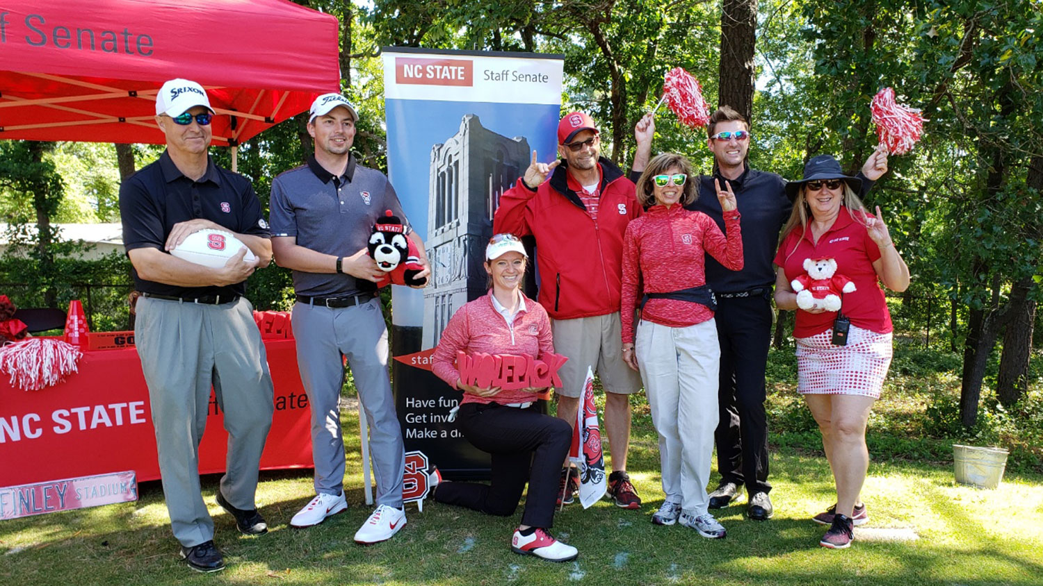 NC State staff pose in front of a red tent at a golf tournament