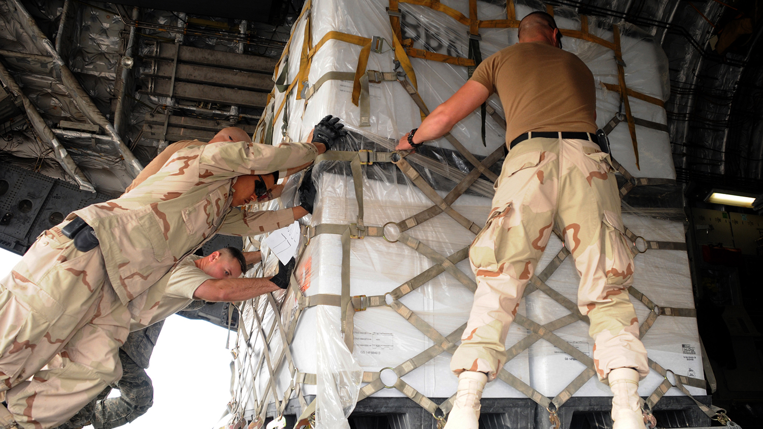 military personnel maneuver equipment into an airplane for transport