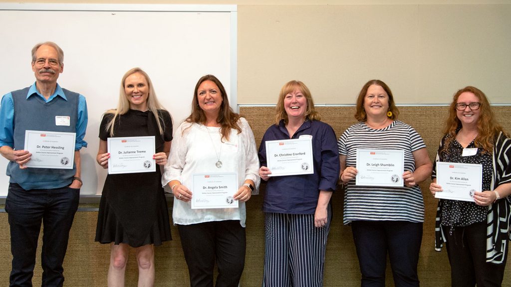 six people standing against a wall holding certificates