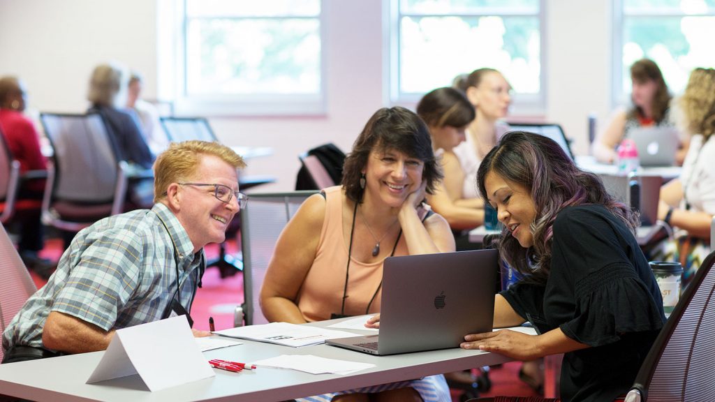 one man and two women sitting around a laptop on a table