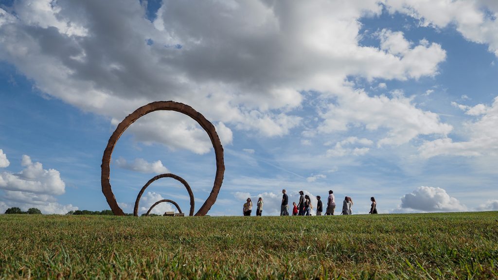 A group of students walks in front of a earthen sculpture at the NC Art Museum park.