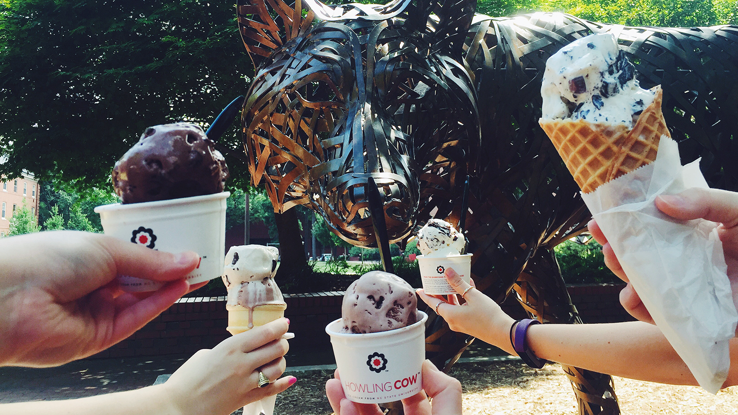 Five hands hold up Howling Cow ice cream scoops near a brass wolf.