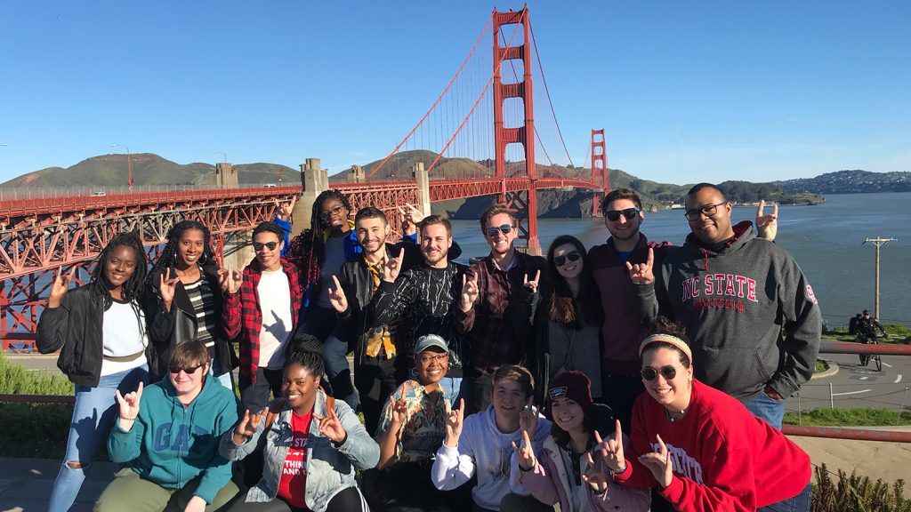 A team of students hold up wolf hands in front of the Golden Gate Bridge in San Francisco