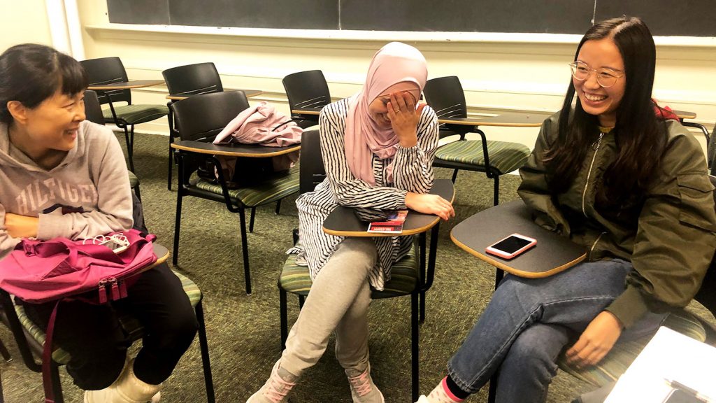 three students sitting at desks, laughing