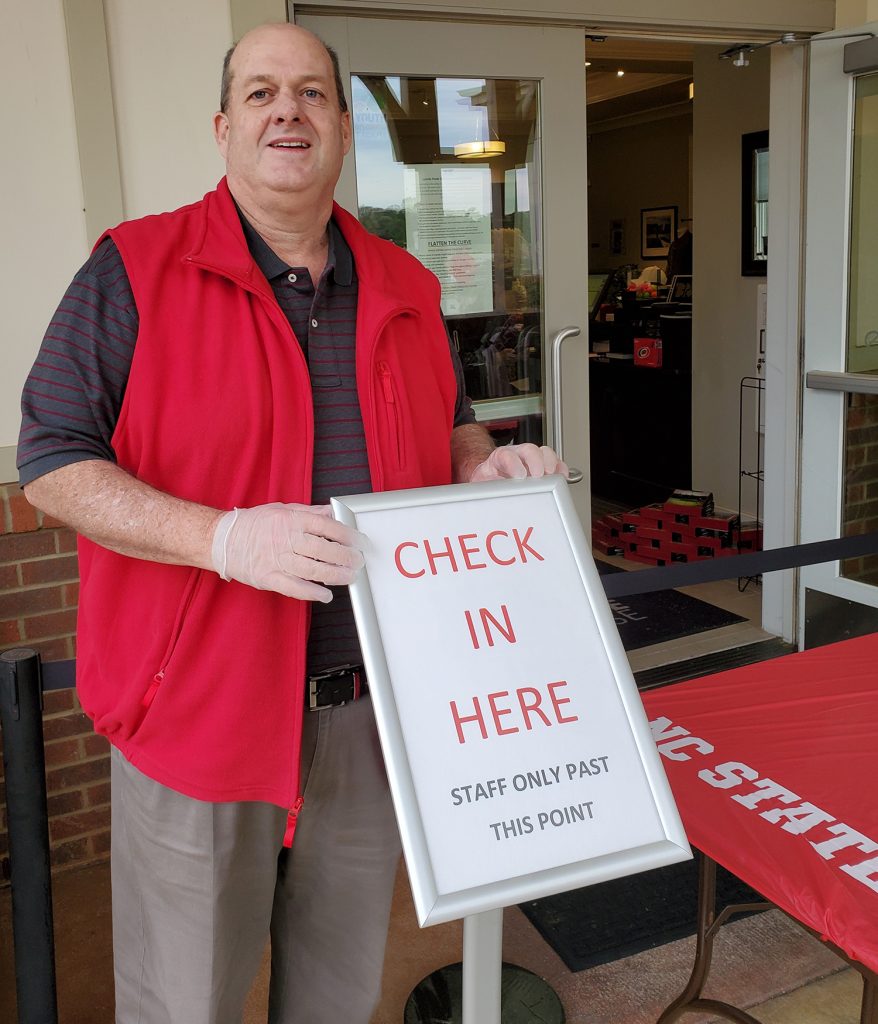 Chip Watson in front of the clubhouse with a sign that says, "Check in Here."