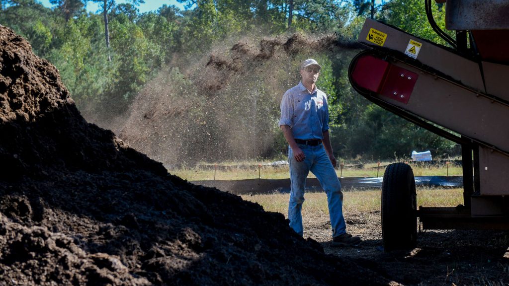 compost being added to a pile with a supervisor in the background