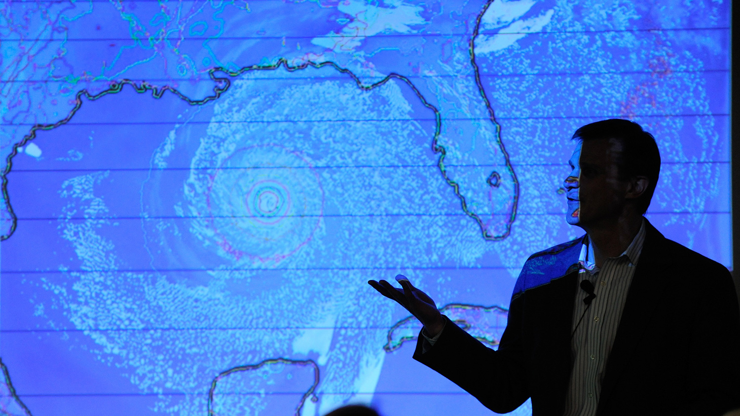 A person silhouetted against a weather map displaying a hurricane