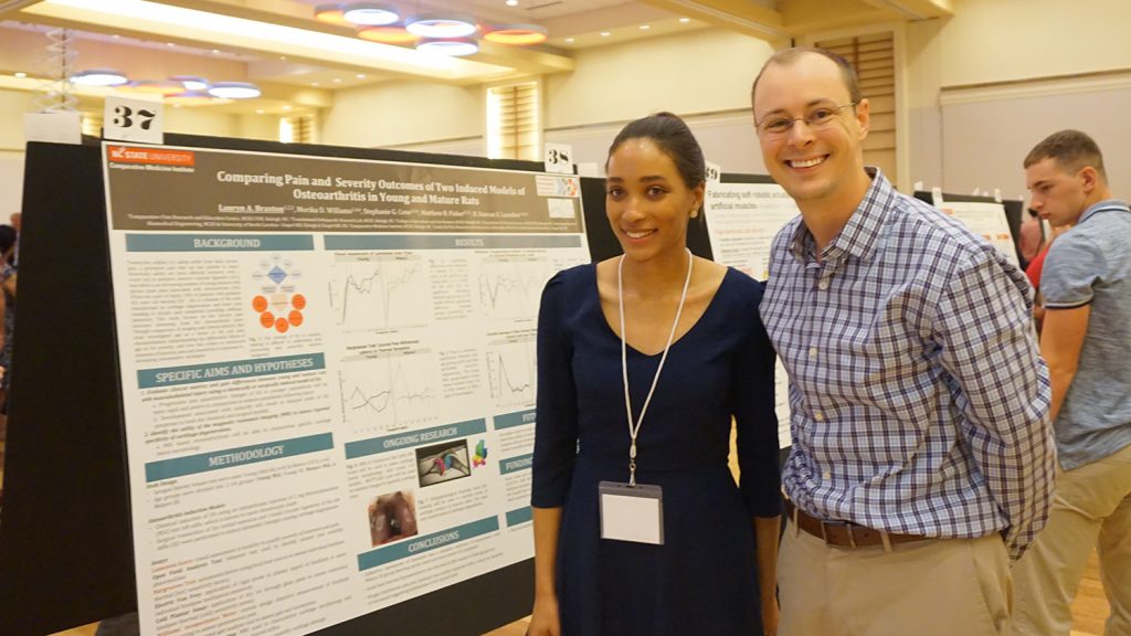 Student Lauryn Braxton and Professor Matt Fisher stand next to Braxton's research poster.