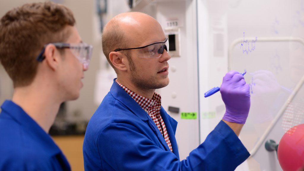 Josh Pierce and a graduate student sketch molecular models on a whiteboard in his lab