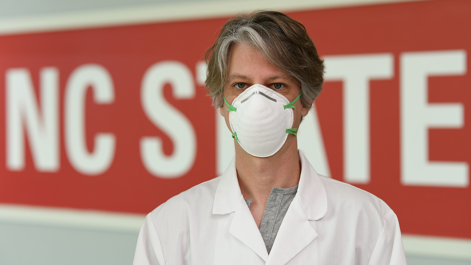 A man wears an N95 mask prototype in front of an NC State banner.