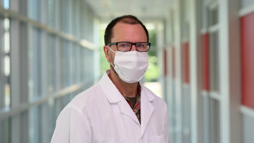 A man wears a surgical mask in a hallway.