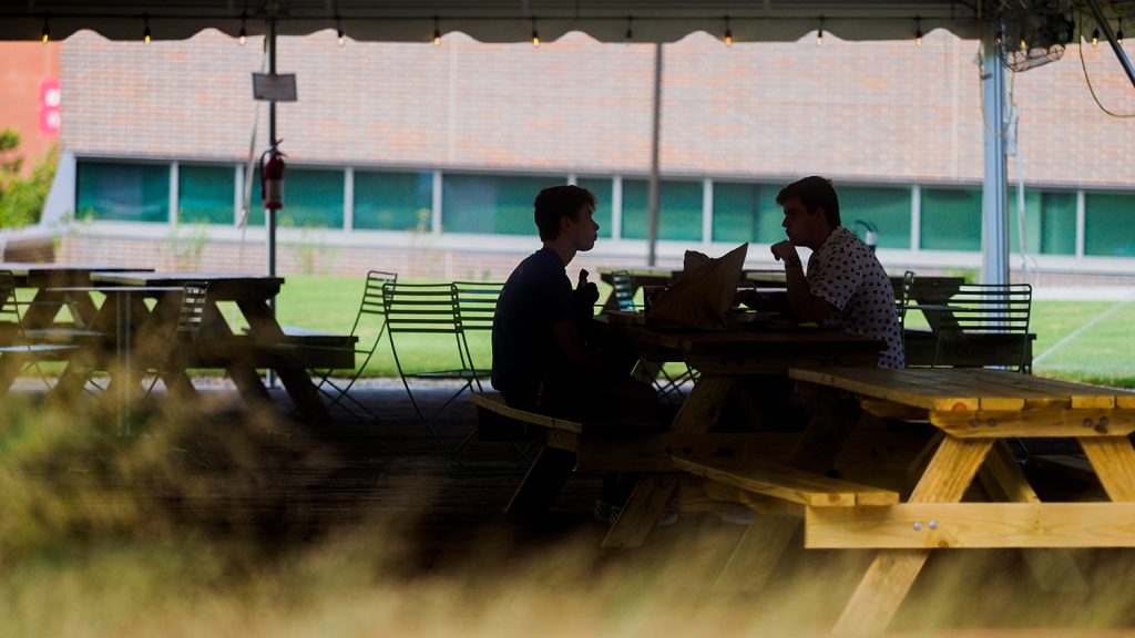 Students eat lunch together at a picnic table under a tent on Centennial Campus's Oval.