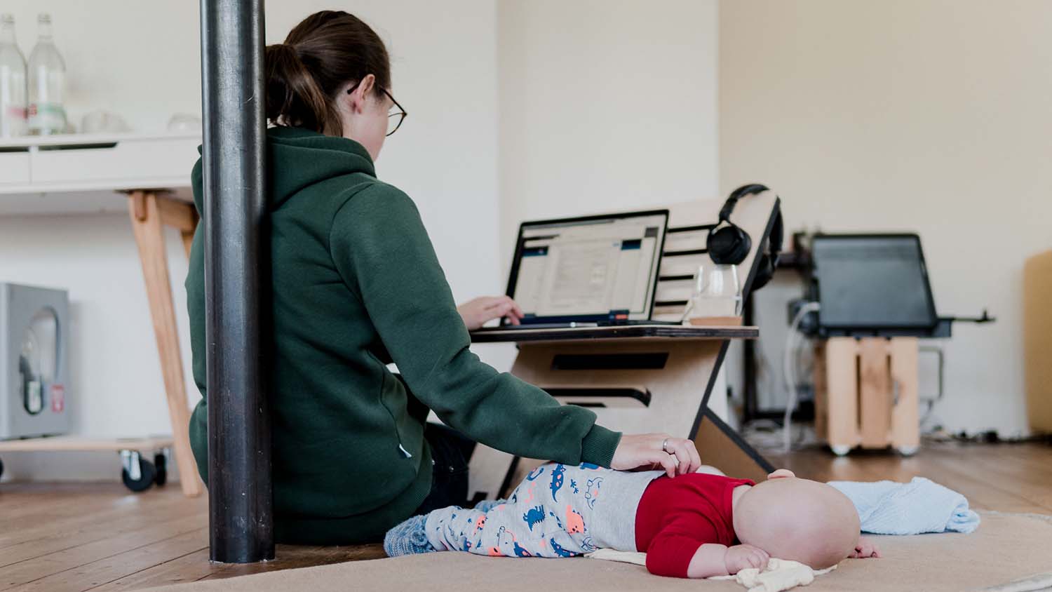 mother pats baby with one hand while working on laptop with another