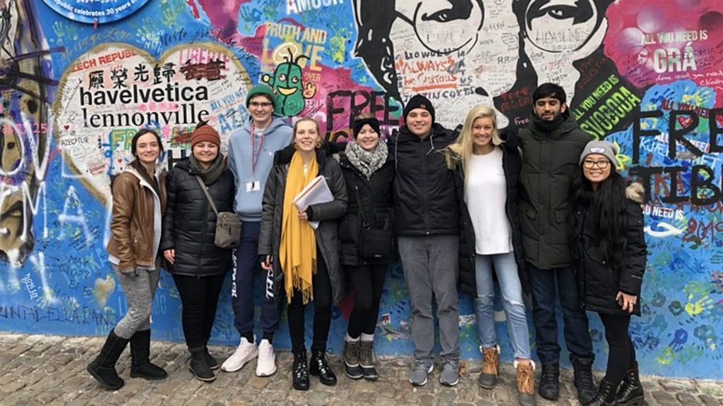 Students pose in front of mural of John Lennon in Prague.