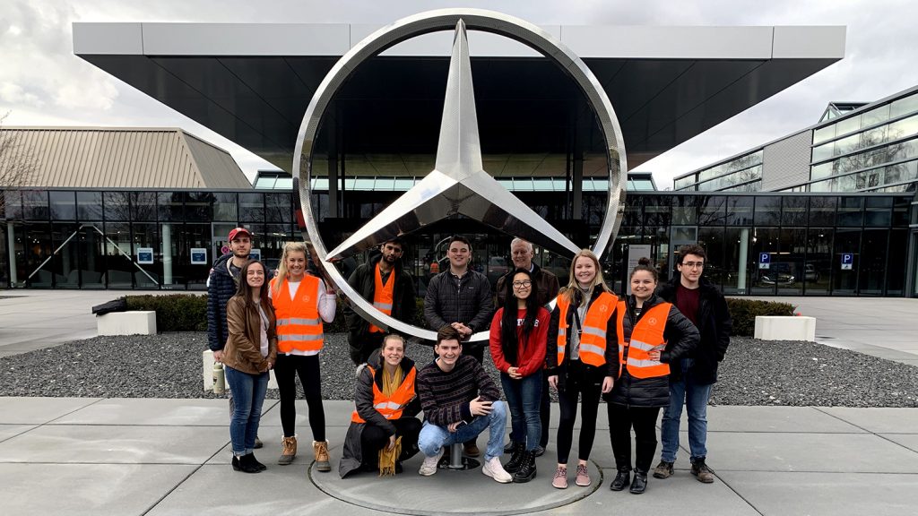 Students pose with a giant Mercedes Benz logo outside the plant in Germany.